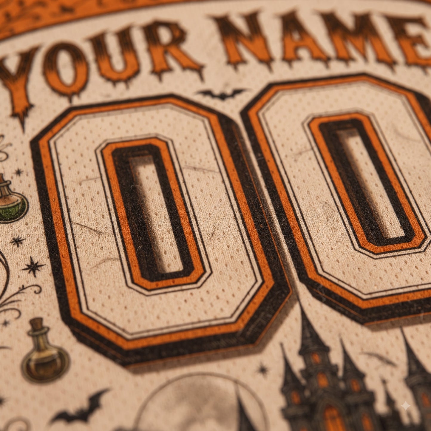 Close-up of a custom printed design featuring large 'YOUR NAME' and '00' text in an orange and black sports-style font on a cream textured background, with Halloween-themed illustrations including bats, a potion bottle, and a castle.