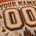 Close-up of a custom printed design featuring large 'YOUR NAME' and '00' text in an orange and black sports-style font on a cream textured background, with Halloween-themed illustrations including bats, a potion bottle, and a castle.