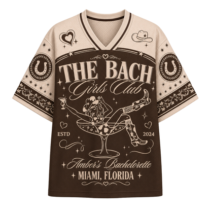 A short-sleeve V-neck t-shirt with a brown and beige graphic design. The design features the text 'THE BACH Girls Club' and 'Amber's Bachelorette Miami, Florida' with a central illustration of a woman in a martini glass.
