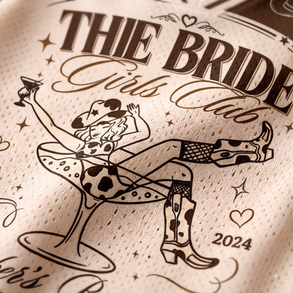 Close-up of a cream-colored mesh fabric printed with a cowgirl-themed graphic and the text 'THIE BRIDE Girls Club 2024' in dark brown.