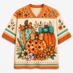 A short-sleeve V-neck t-shirt featuring a colorful autumn-themed graphic print with pumpkins, flowers, acorns, and bows on a cream background with orange and teal stripes.