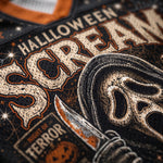 Close-up of a black perforated graphic print featuring distressed cream lettering that reads 'HALLOWEEN SCARE' with an illustrated ghost-face figure holding a knife and a small 'NIGHT OF TERROR' label.