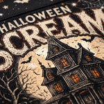 A close-up of a Halloween-themed graphic print featuring a spooky haunted house, bare trees, bats, and the words 'HALLOWEEN SCARE' in distressed cream lettering on a dark background.