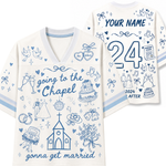 White V-neck t-shirt with blue line art and text, shown in front and back views. The front reads 'going to the Chapel' with wedding-themed doodles like a church, cake, rings, and champagne glasses.