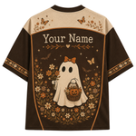 A short-sleeve t-shirt with a Halloween-themed graphic print on the back. The design features a cream-colored upper yoke with butterfly and floral motifs, a dark brown lower body, and a central illustration of a cute ghost wearing an orange bow and holding a jack-o'-lantern basket, surrounded by flowers and the text 'Your Name'.