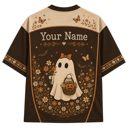 A short-sleeve t-shirt with a Halloween-themed graphic print on the back. The design features a cream-colored upper yoke with butterfly and floral motifs, a dark brown lower body, and a central illustration of a cute ghost wearing an orange bow and holding a jack-o'-lantern basket, surrounded by flowers and the text 'Your Name'.