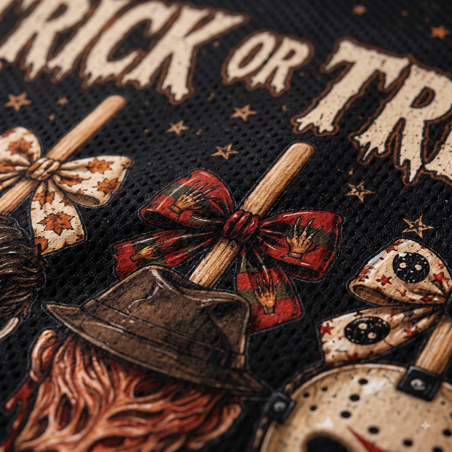 Close-up of a black mesh fabric printed with a horror-themed 'Trick or Treat' design, featuring a brown fedora hat, red patterned bows, wooden sticks, and distressed cream text.
