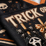 Close-up of a black mesh fabric with Halloween-themed graphics, including the words “TRICK OR TREAT,” skulls, stars, and decorative bows in beige, orange, and black.