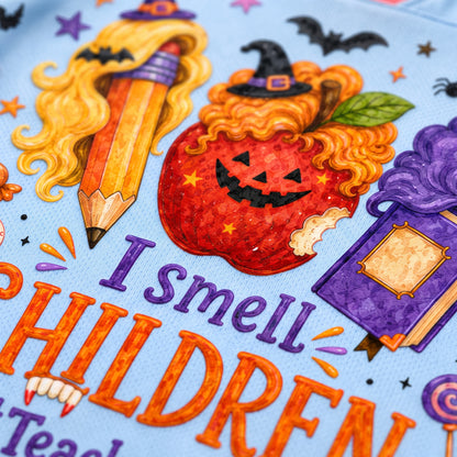Close-up of a light blue fabric featuring a colorful Halloween-themed graphic with the text 'I smell CHILDREN' in orange and purple, surrounded by illustrated elements including a pencil with curly blonde hair, a jack-o'-lantern apple, a purple potion bottle, bats, and stars.
