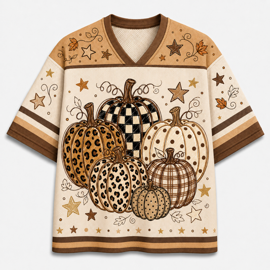 A short-sleeve V-neck t-shirt featuring a fall harvest design with illustrated pumpkins in leopard, checkered, polka-dot, and plaid patterns, along with stars and leaves on a cream background with brown trim.