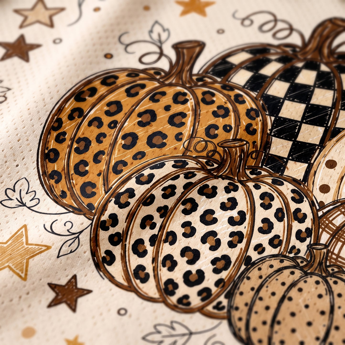 Close-up of a pumpkin print pattern on a textured fabric, featuring illustrated pumpkins with leopard print, checkered pattern, and polka dots in beige, brown, black, and white.