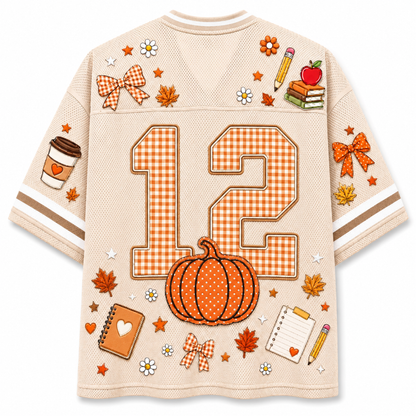 A beige mesh sports jersey with orange and white gingham details, featuring the number 12, a pumpkin, autumn leaves, bows, and school-themed illustrations on the back.