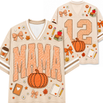 A beige football-style jersey shown from the front and back, decorated with autumn and school-themed graphics including a pumpkin, bows, leaves, notebooks, pencils, an apple, and the word “MAMA” in gingham letters. The back shows the number 12.