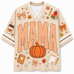 A beige short-sleeve V-neck jersey-style shirt with orange and white gingham lettering that says “MAMA,” decorated with autumn-themed graphics including a pumpkin, bows, stars, flowers, a coffee cup, notebooks, and pencils on a plain white background.