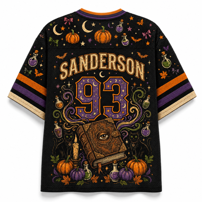 A black short-sleeve t-shirt with a vibrant Halloween-themed graphic print featuring the name 'SANDERSON' and number '93' on the back. The design includes pumpkins, bats, stars, potion bottles, a witch's eye book, and crescent moons, with orange, purple, and gold striped sleeves.