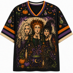 A black V-neck t-shirt featuring a detailed graphic print of the three Sanderson sisters from The Sandman, surrounded by Halloween motifs like pumpkins, cauldrons, and bats, with orange and purple striped sleeve accents.