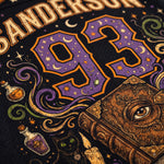 Close-up of a black sports jersey featuring a large purple and gold number 93 with moon and star motifs, surrounded by decorative illustrations including a book with an eye, potion bottles, a cat, and the name SANDERSON.