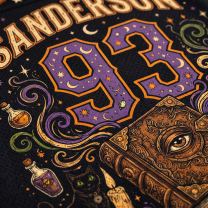 Close-up of a black sports jersey featuring a large purple and gold number 93 with moon and star motifs, surrounded by decorative illustrations including a book with an eye, potion bottles, a cat, and the name SANDERSON.