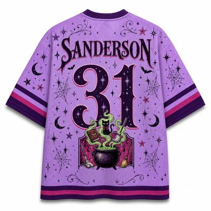 A purple short-sleeve jersey-style shirt shown from the back, featuring the name SANDERSON and the number 31 in large decorative lettering. The design includes a witch illustration with a cauldron, green smoke, stars, moons, bats, and spiderwebs, plus pink and purple striped sleeve and hem accents.