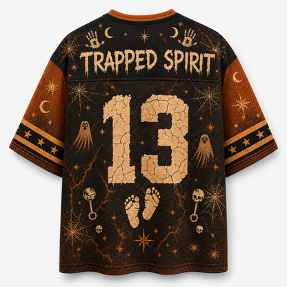 A short-sleeve graphic T-shirt shown from the back, featuring a dark brown and black Halloween-themed design with the words 'TRAPPED SPIRIT,' a large cracked beige number 13, ghosts, stars, moons, footprints, and spiderwebs. The shirt is photographed on a plain light background.