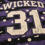 Close-up of a purple and black graphic fabric featuring the word 'WICKED' in distressed cream lettering above the number '31' in cream with purple outlines, decorated with cream stars and dots.